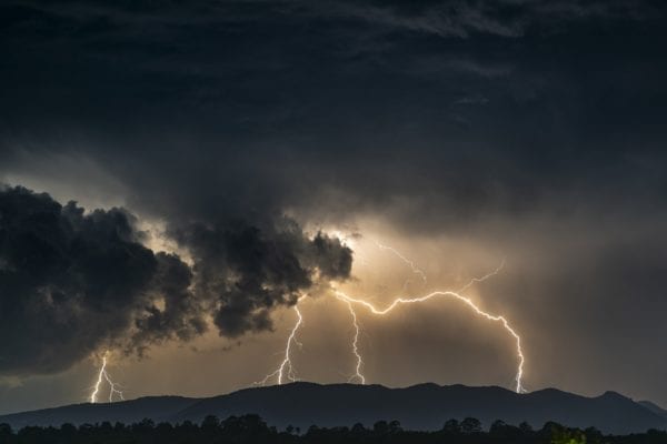 a black cloud with lightning striking a mountain