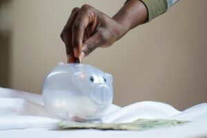 A hand is putting a coin into a piggy bank, representing savings.